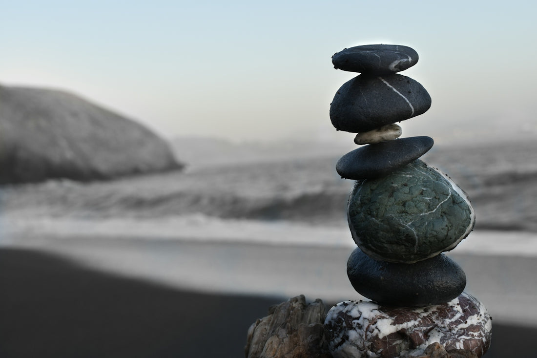 A stack of smooth dark stones on a beach with a blurred coastline