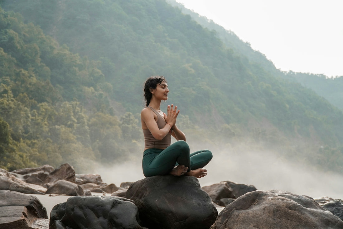a woman sitting on top of a rock next to a river