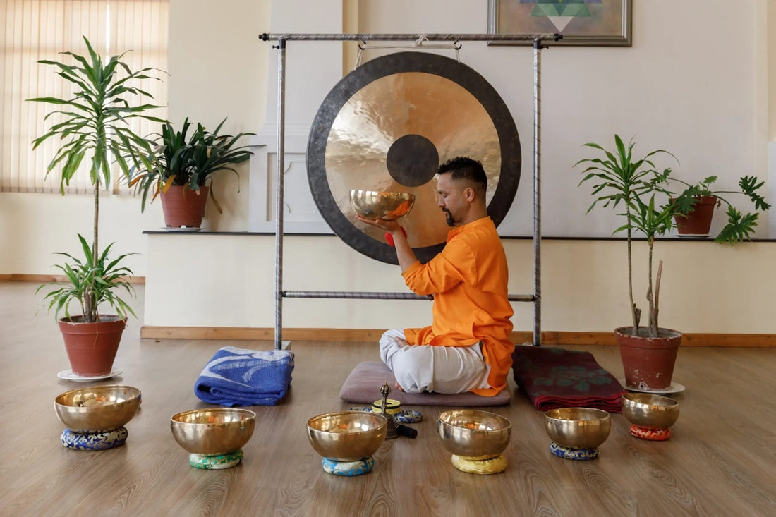 Man playing a large gong with singing bowls around him